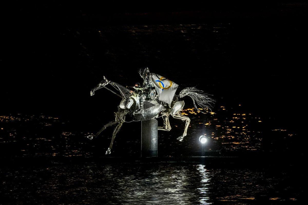 La doncella en armadura, con la bandera olímpica sobre un caballo mecánico / Foto: AP